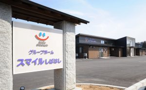 施設の外観と看板。白いブロック造りの建物と駐車場が見える。